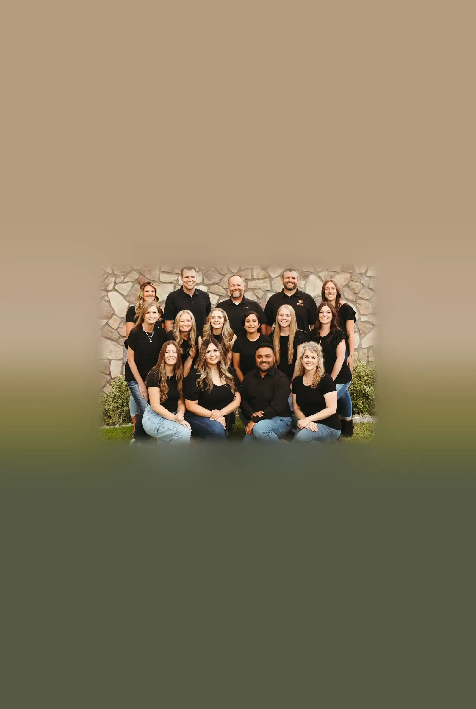 Dental team members wearing black shirts and jeans posing together outdoors in front of a stone wall.